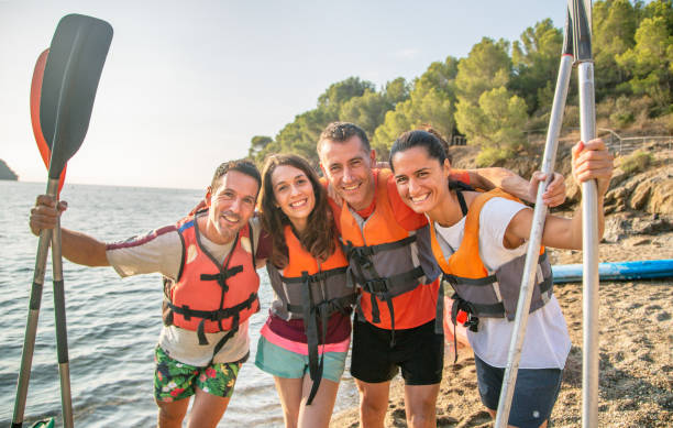 Portrait of Kayaking Friends Holding Paddles on Beach Close-up of smiling male and female friends in 30s and 40s embracing and holding paddles after kayaking in Mediterranean. sea kayak stock pictures, royalty-free photos & images