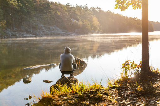 A Latino man is sitting on a rock and is looking out over a lake.