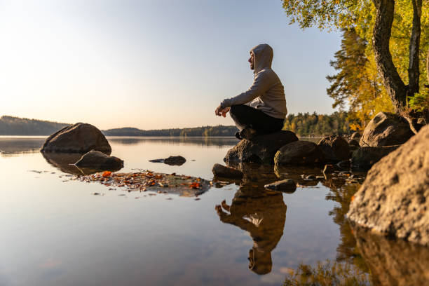 A Latino man is is sitting in crossed-leg position on a rock and is looking out over a lake.
