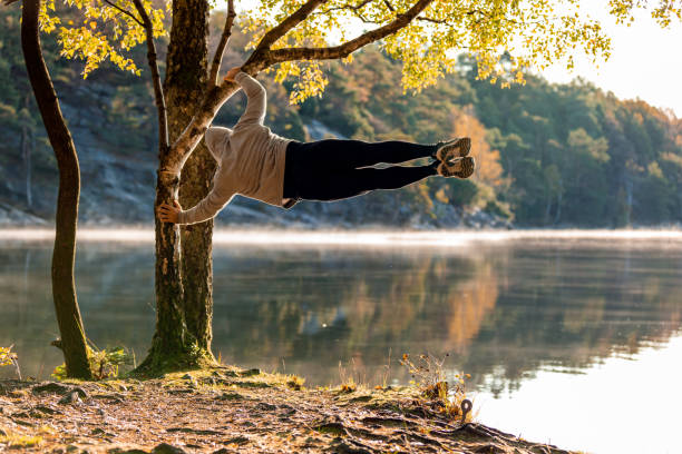 Man exercising outdoors A Latino man is hanging from a tree, he is doing the human flag. He is in a forest in front of a lake. nature reserve photos stock pictures, royalty-free photos & images