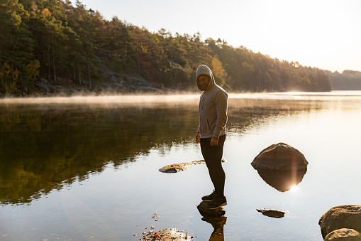A Latino man is standing on a rock and is looking out over a lake.