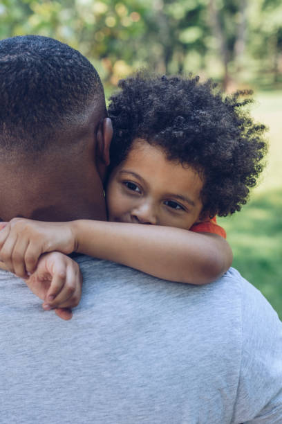istock adorable african american boy hugging father while walking in park 1180156534