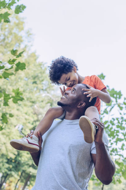 happy african american man piggybacking adorable son while walking in park happy african american man piggybacking adorable son while walking in park preschool student photos stock pictures, royalty-free photos & images