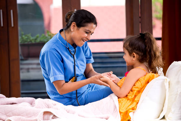 Female nurse having fun with girl lying on bed during medical house call Female nurse having fun with girl lying on bed during medical house call india hospital stock pictures, royalty-free photos & images