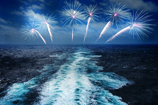 splashing waves in ocean with fireworks display in night sky, celebration concept