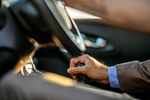 Businessman driving his car on background. Close-up human hand holding gear shift knob. Not faster than life. Unrecognizable Business man driving car.