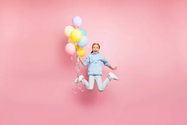 Photo of Full length body size photo of cheerful positive cute nice screaming funny comic girl holding balloons with hands shouting flying jumping in blue sweatshirt sweater hoodie jeans denim isolated pastel color background