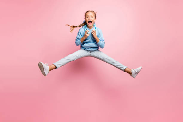 volle länge foto von hübschen kleinen dame springen hoch aufgeregt sommer stimmung hören moderne ohrklappen playlist tragen lässige kleidung isoliert rosa farbe hintergrund - child bizarre little girls humor stock-fotos und bilder