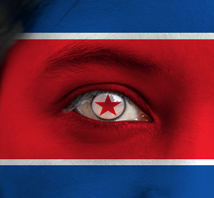 Human face painted North Korea flag with red star within a white circle on the center of eye or eyeball. Human eye painted with flag of Democratic People's Republic of Korea.