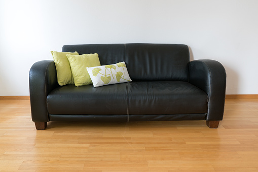 A horizontal view of a dark brown leather couch with three pillows in a minimalist apartment