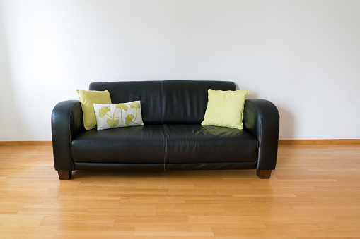 A horizontal view of a dark brown leather couch with three pillows in a minimalist apartment