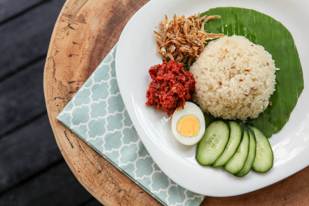 Simple Dish of Malaysian Nasi Lemak Nasi lemak or fragrant rice dish cooked in coconut milk and pandan leaf, commonly found in Malaysia and considered as the national dish. It is also a native dish in neighbouring countries with significant Malay population. Image shows nasi lemak with hard boiled egg, sambal, fried anchovies, sliced cucumber, marinated fried prawn. It is traditionally served with cut banana leaf spread or wrapped in it. traditional malaysian food stock pictures, royalty-free photos & images