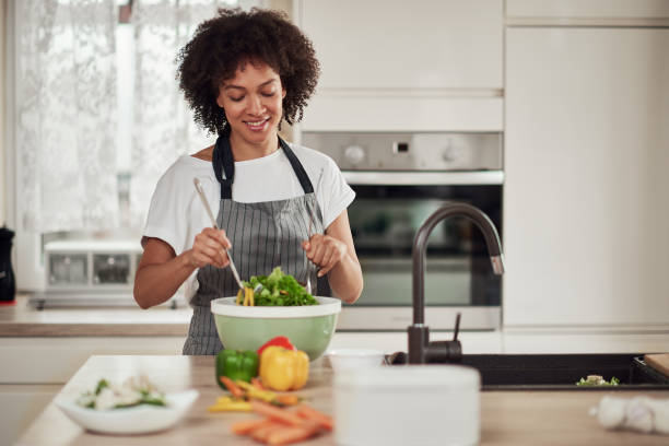 istock Woman mixing vebgetables in bowl while standing in kitchen. 1180169530