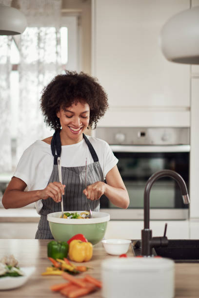 istock Woman mixing vebgetables in bowl while standing in kitchen. 1180170482