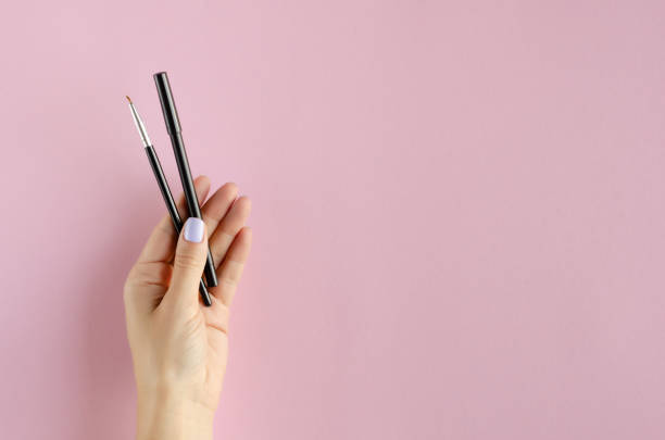 istock Hand with makeup brush and pencil composition on pink background. 1180170809