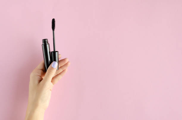 istock Hand with black mascara composition on pink background. 1180170863