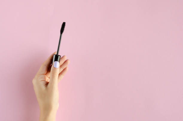istock Hand with black mascara composition on pink background. 1180170874