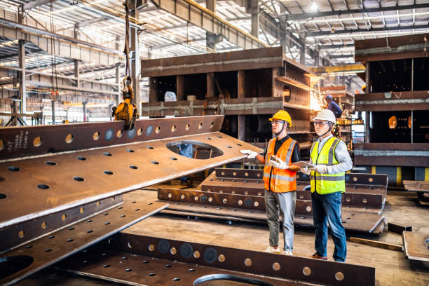Two metal workers operating a crane in a steel factory Two metal workers operating a crane to move steel members. crane machinery stock pictures, royalty-free photos & images