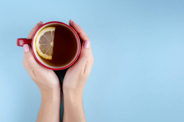 istock Hand with red tea cup and lemon slice composition on blue background. 1180172054