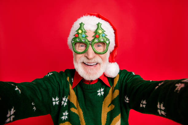 closeup photo of funny aged santa claus role man making crazy selfies wear x-mas tree shape specs knitted sweater hat isolated red background - natal fotos imagens e fotografias de stock