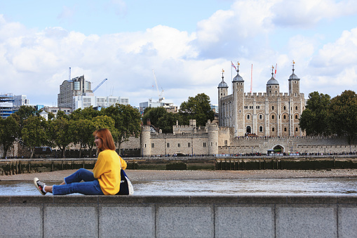 London, UK - August 20, 2019: A young Japanese Asian tourist playfully poses for the camera\nOne of London's most famous landmarks, the historic Tower houses the Crown Jewels, the prison cell of Sir Walter Raleigh, known as the Bloody Tower, and the Chapel of St. John and the Royal Armories.