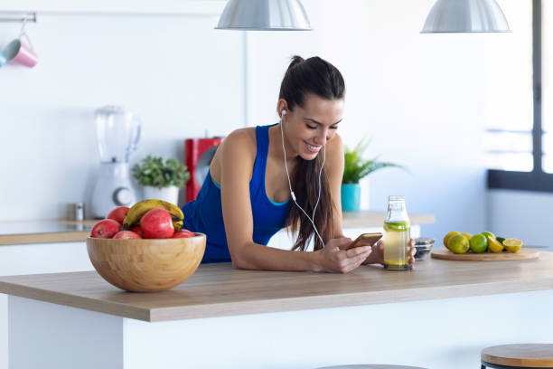 jeune femme sportive écoutant la musique avec le téléphone portable après formation dans la cuisine à la maison. - healthy eating sport exercising women photos et images de collection