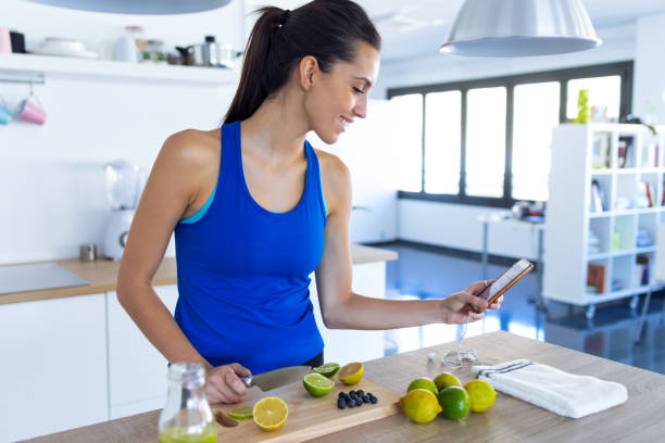 istock Sporty young woman using her mobile phone while cutting limes for preparing detox beverage in the kitchen at home. 1180177449