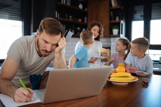 istock Man going through bills with family behind him 1180179015