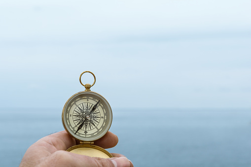 Man holds a compass against the horizon of the sea one day with fog