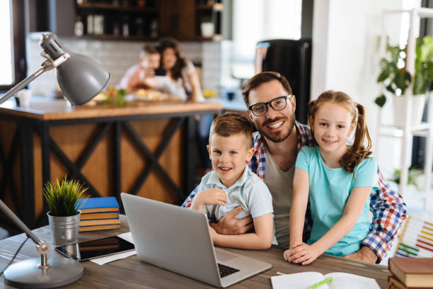 istock Father with daughter and son on his lap using laptop at home 1180180431