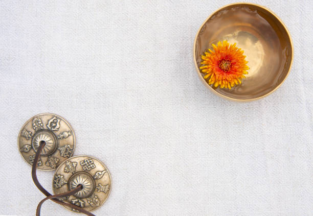 istock A small singing bowl stands in the upper right corner filled with water with floating chrysanthemum inside. A small singing bowl and tingsha stand on a gray background of organic cotton. Top view. 1180187224