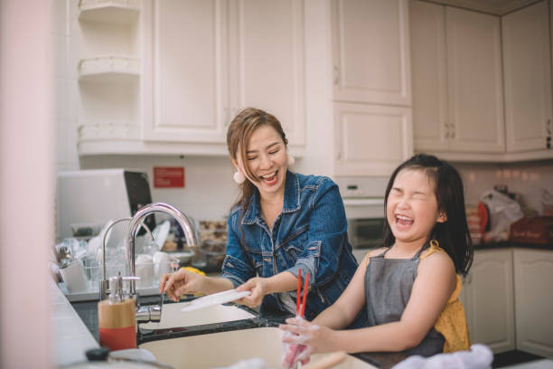 una madre cinese asiatica lavare i piatti con sua figlia in cucina e divertirsi legando - wash stand foto e immagini stock