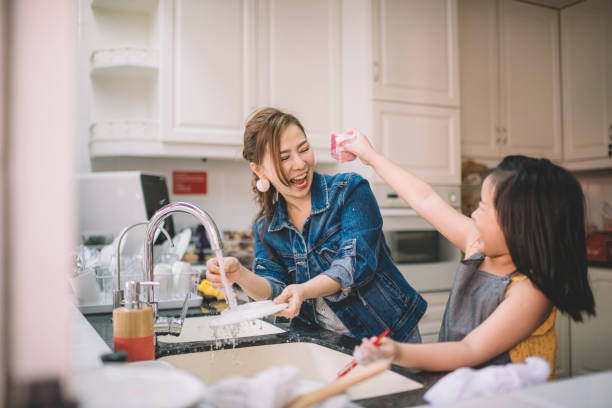 una madre china asiática lavando platos con su hija en la cocina y divirtiéndose enlazando - lavar los platos fotografías e imágenes de stock