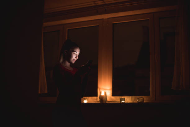 hermosa mujer usando el teléfono en la habitación oscura - window light window sill home interior fotografías e imágenes de stock