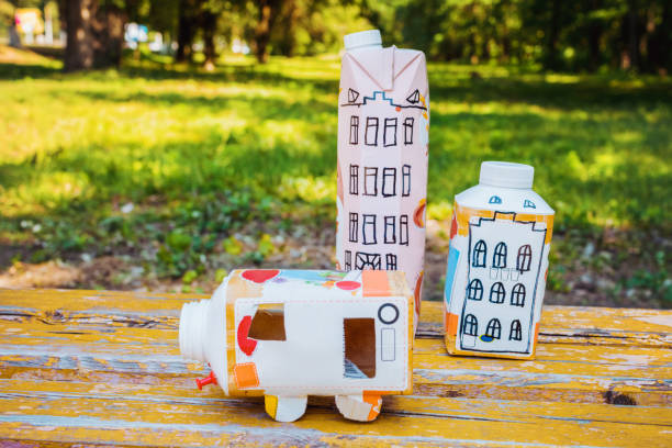 Houses and toy cars made from milk bags on grass. DIY paper milk bag. Creative paper milk bag ideas. Recycle crafts. stock photo