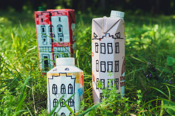 Houses and toy cars made from milk bags on grass. DIY paper milk bag. Creative paper milk bag ideas. Recycle crafts. stock photo