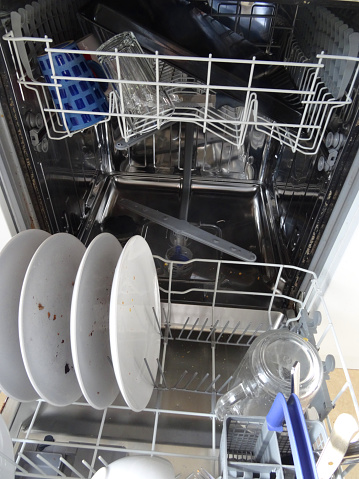 Stock photo showing an open dishwasher half loaded with dirty crockery, cutlery and pans.