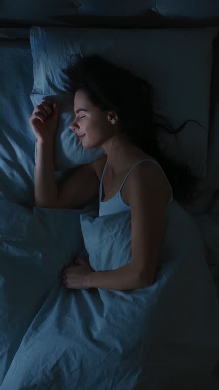 Top View of Beautiful Young Woman Sleeping Cozily on a Bed in His Bedroom at Night. Vertical Screen Orientation Video 9:16