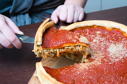 Vista superior de la pizza de Chicago. Mujer manos cortando estilo Chicago plato profundo pizza de queso italiano con salsa de tomate y carne de res se encuentran en el interior photo