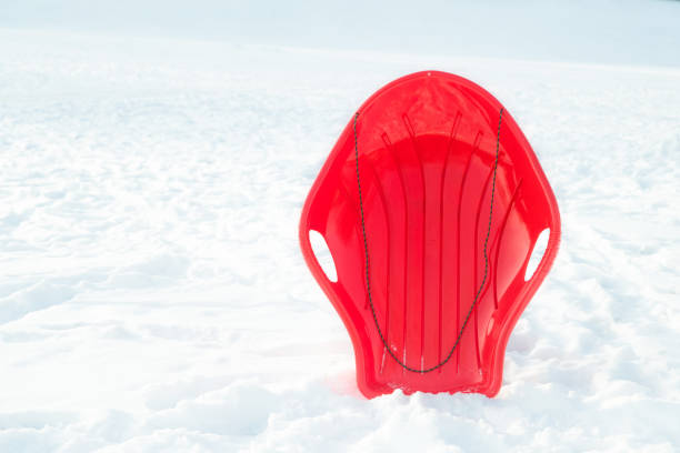 Red plastic sleigh, sledge, sled on white snowy background outdoors. Winter play and activity for kids