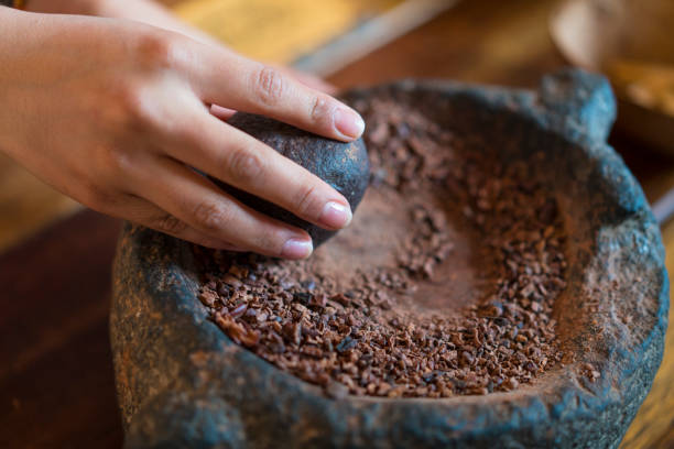 A woman with a stone grinder grinds cocoa and prepares cacao for a chocolate drink, Ecuador stock photo