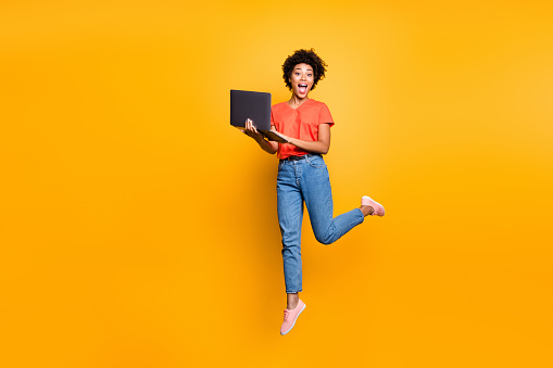 Full size photo of amazed crazy curly brown hair girl use her laptop have notification in feednews jump scream omg wear denim, jeans red t-shirt lifestyle sneakers isolated yellow color background