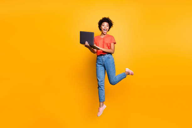 Full size photo of amazed crazy curly brown hair girl use her laptop have notification in feednews jump scream omg wear denim jeans red t-shirt lifestyle sneakers isolated yellow color background Full size photo of amazed crazy curly brown hair girl use her laptop have notification in feednews jump scream omg wear denim, jeans red t-shirt lifestyle sneakers isolated yellow color background jumping stock pictures, royalty-free photos & images