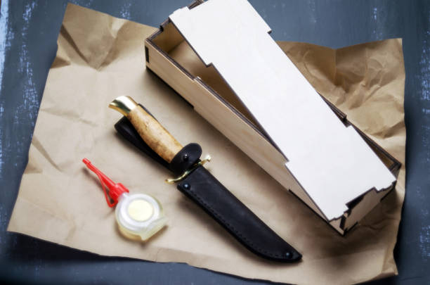 Knife with a fixed handle in a gift box with leather sheath and oil for impregnation on paper and a dark background.