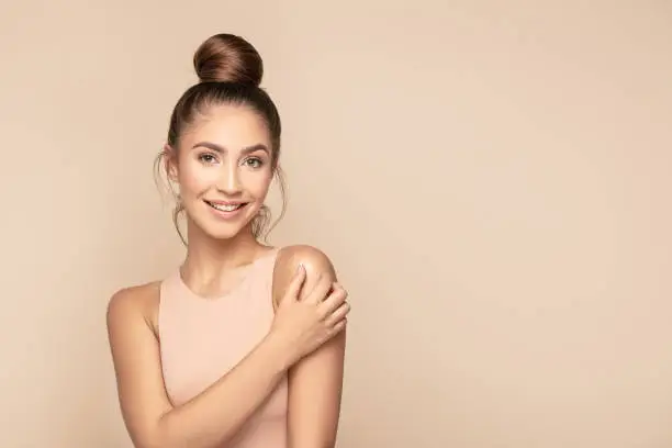 Beauty feminine portrait of female face with healthy natural skin. Beautiful tanned girl with brown hair looking at camera. Pretty attractive young woman posing at studio on beige studio background.