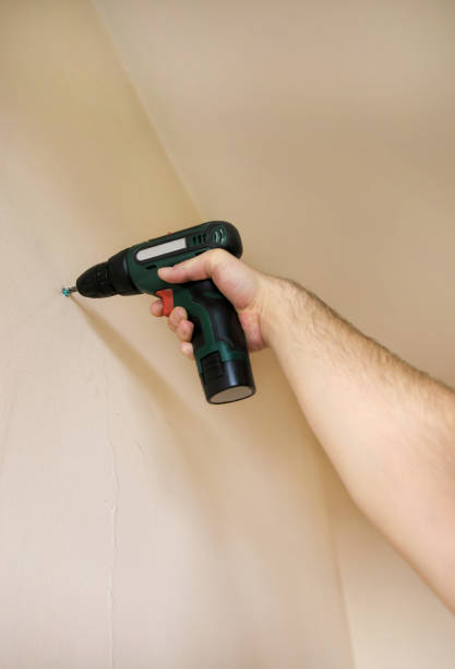 Construction worker and handyman works on renovation of apartment. Builder using electric screwdriver and screwing screw out of wall on construction site. Home renovation concept. Construction tool. trabajador de la construcción y manitas trabaja en la renovación del apartamento. constructor usando destornillador eléctrico y atornillando tornillo fuera de la pared en el sitio de construcción. concepto de renovación del hogar. herramienta de const