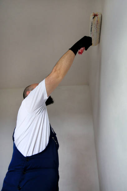 istock Construction worker doing finish renovation at apartment. Professional painter contractor using white paint roller brush painting of concrete wall room on construction site. Home renovation concept. 1180213197
