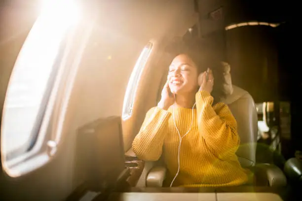 Young fashionable woman sitting in a private jet and listening to music through the headphones.