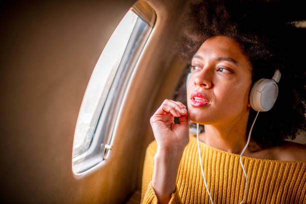 istock Young chic woman sitting on a private jet and looking through a window while listening to music through headphones 1180214058