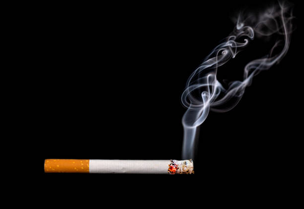 istock Close up of a cigarette with smoke showing at black background 1180214655